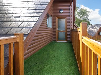 A balcony with green artificial grass flooring wooden railing and a glass door at Classic Lodge 30 in Dyserth