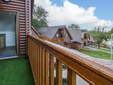 A balcony with wooden railing overlooking a row of brown wooden lodges and a pathway at Classic Lodge 30 in Dyserth