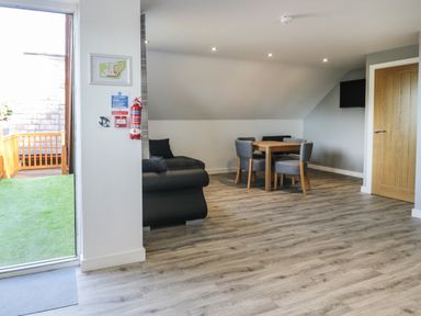 A room with a wooden dining table and four chairs a black sofa a wall-mounted tv and a door leading outside at Classic Lodge 30 in Dyserth