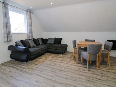 A room with a dark sofa and a wooden dining table with four chairs at Classic Lodge 30 in Dyserth