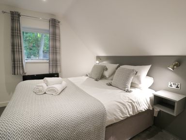 A bedroom with a bed with white linens and gray pillows next to a window with plaid curtains at Classic Lodge 30 in Dyserth