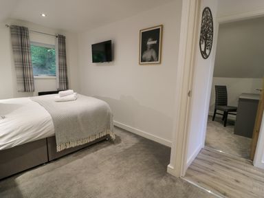 A bedroom with a bed, wall-mounted TV, framed picture, and an adjoining room with a desk and chair at Classic Lodge 30 in Dyserth