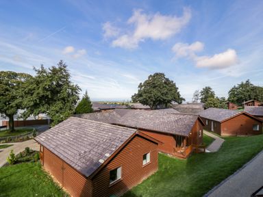 Several wooden lodges with pitched roofs on green lawns and trees under a blue sky at Classic Lodge 30 in Dyserth