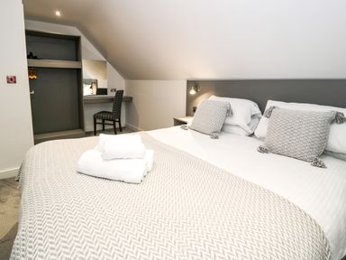 A bedroom with a double bed two patterned pillows folded towels desk chair and open closet at Classic Lodge 30 in Dyserth