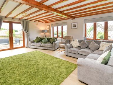 A living room with two grey sofas a green rug wood beam ceiling and large windows at Pondarosa in Newbridge-On-Wye