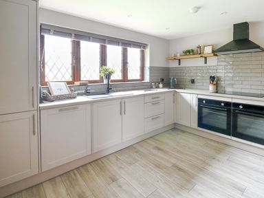 A kitchen with white cabinets grey subway tile backsplash a large window and double ovens at Pondarosa in Newbridge-On-Wye