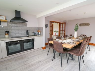 A kitchen with double oven stove and dining table set for ten with brown chairs at Pondarosa in Newbridge-On-Wye