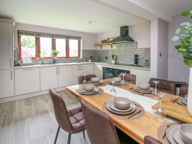 A kitchen with white cabinets a wooden dining table set with plates bowls and glasses at Pondarosa in Newbridge-On-Wye