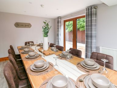 A dining room with a wooden table set with plates bowls glasses and cutlery and a vase with greenery at Pondarosa in Newbridge-On-Wye