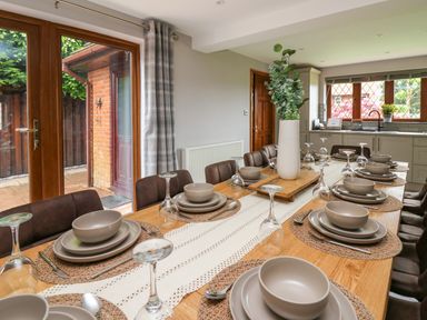 A dining room with a long wooden table set with plates bowls cutlery and upside down wine glasses and a vase with greenery at Pondarosa in Newbridge-On-Wye
