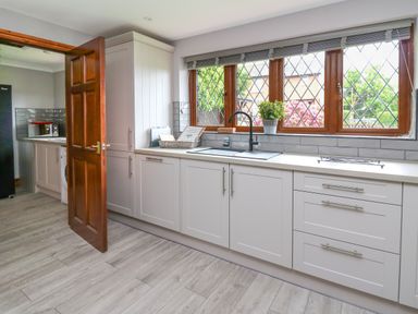A kitchen with white cabinets a sink below a window and a wooden door leading to another room at Pondarosa in Newbridge-On-Wye