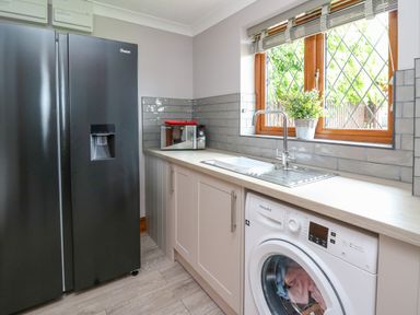 A utility room with a black fridge freezer a microwave a washing machine a sink and a window with blinds and a plant on the sill at Pondarosa in Newbridge-On-Wye