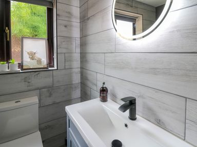A bathroom with a sink and faucet a round illuminated mirror a toilet and two small plants on a windowsill at Pondarosa in Newbridge-On-Wye
