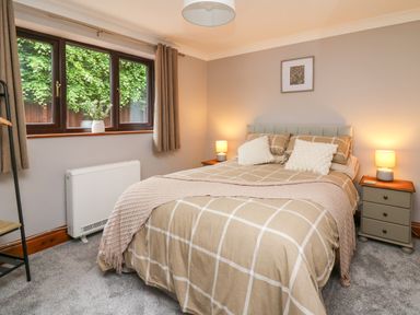 A bedroom with a bed with checked bedding two bedside tables with lamps a window with curtains and a framed picture on the wall at Pondarosa in Newbridge-On-Wye