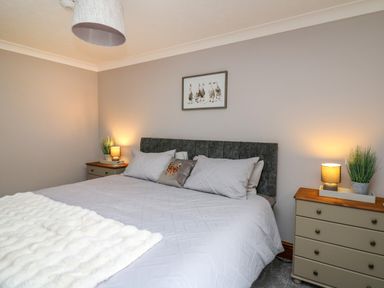 A bedroom with a double bed between two nightstands with lamps and plants and a picture of ducks on the wall at Pondarosa in Newbridge-On-Wye