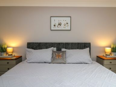 A bedroom with a bed with white bedding and pillows a framed picture of birds above and two bedside tables with lamps and plants at Pondarosa in Newbridge-On-Wye