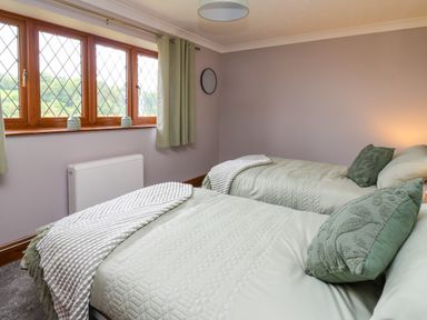 A bedroom with two single beds green bedding and cushions a window with green curtains and a radiator below at Pondarosa in Newbridge-On-Wye