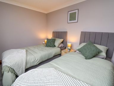 A bedroom with two single beds green bedding wooden nightstand between beds with lamps and framed picture on wall at Pondarosa in Newbridge-On-Wye