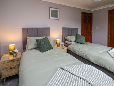 A bedroom with two single beds side by side each with a headboard and green bedding with bedside tables and lamps at Pondarosa in Newbridge-On-Wye