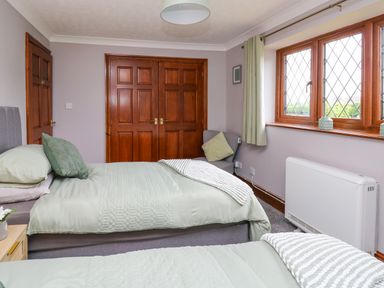 A bedroom with two single beds green bedding wooden doors a gray chair near window with curtains at Pondarosa in Newbridge-On-Wye