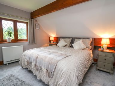 A bedroom with a double bed two bedside tables with lamps and a window with curtains at Pondarosa in Newbridge-On-Wye