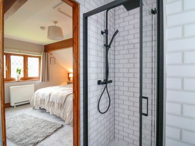 A bathroom with a black framed glass shower next to a bedroom with a bed a window and curtains at Pondarosa in Newbridge-On-Wye