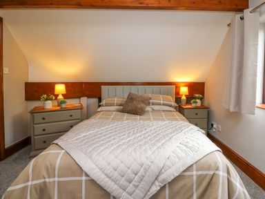 A bedroom with a double bed two bedside tables with lamps and plants and a window with curtains at Pondarosa in Newbridge-On-Wye