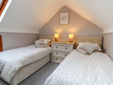 A bedroom with two single beds separated by a three-drawer dresser with two lamps and a framed wall art at Pondarosa in Newbridge-On-Wye