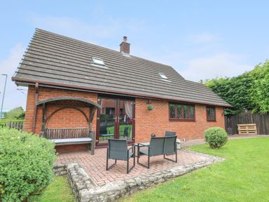A brick house with a sloped roof and skylights with outdoor seating on a paved patio in a garden at Pondarosa in Newbridge-On-Wye