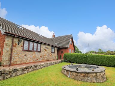 A stone and brick house with a sloped roof next to a circular stone structure in a grass yard at Pondarosa in Newbridge-On-Wye