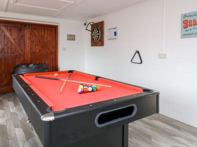 A game room with a pool table, pool cues, dartboard, bean bag, and wooden double doors at Pondarosa in Newbridge-On-Wye