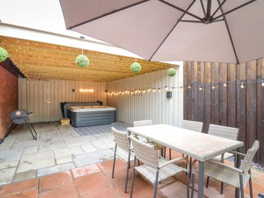 An outdoor covered patio with a hot tub a dining table six chairs a grill and string lights at Pondarosa in Newbridge-On-Wye