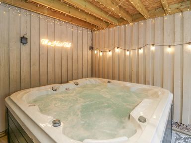 An indoor hot tub with bubbling water under a wooden ceiling and walls with string lights and a neon sign that says The Hot Tub at Pondarosa in Newbridge-On-Wye