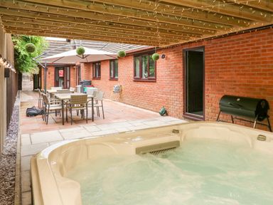 An outdoor covered patio with a hot tub dining table and chairs a large umbrella and a barbecue grill at Pondarosa in Newbridge-On-Wye