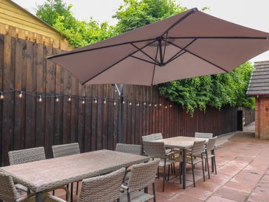 An outdoor patio area with two rectangular tables and chairs under a large umbrella at Pondarosa in Newbridge-On-Wye