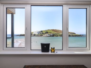 A window with a view of the sea and an island with buildings and grassy hills at 14 Burgh Island Causeway in Bigbury-On-Sea