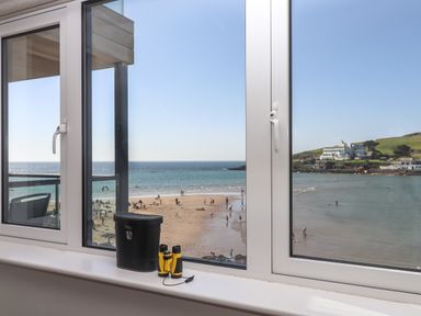 A window view of a beach with people on the sand and a body of water with buildings on a hill at 14 Burgh Island Causeway in Bigbury-On-Sea