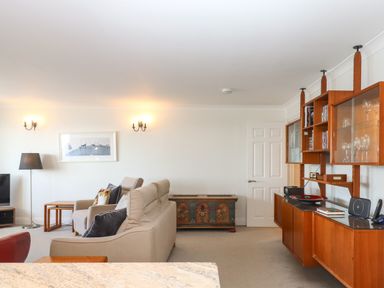A living room with beige sofas a wooden cabinet glassware a floor lamp and a TV at 14 Burgh Island Causeway in Bigbury-On-Sea