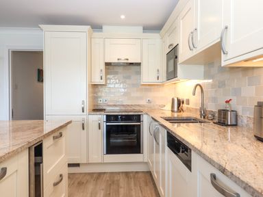 A kitchen with white cabinets granite countertops oven dishwasher microwave kettle and wooden floor at 14 Burgh Island Causeway Bigbury-On-Sea
