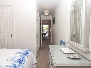 A hallway with a glass top dresser and mirror on the right and a bed with a blue and white cover on the left at 14 Burgh Island Causeway in Bigbury-On-Sea
