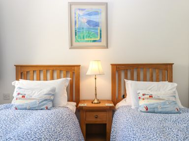 A bedroom with two single beds with wooden headboards a wooden nightstand with a lamp and a painting on the wall at 14 Burgh Island Causeway in Bigbury-On-Sea