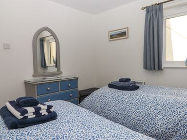 A bedroom with two single beds blue patterned bedspreads blue dresser with mirror and blue curtains at 14 Burgh Island Causeway Bigbury-On-Sea