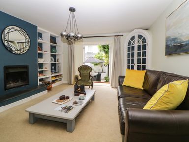 A living room with a brown leather sofa with yellow cushions a green armchair a coffee table a fireplace and built in shelves at Lower Culvermead in Chaddlehanger near Tavistock