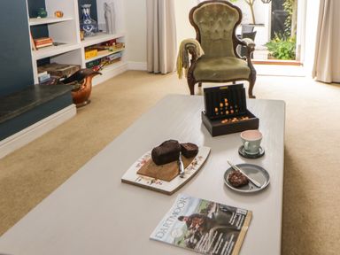 A living room with an armchair and coffee table with cake cup plate game and magazine at Lower Culvermead in Chaddlehanger near Tavistock