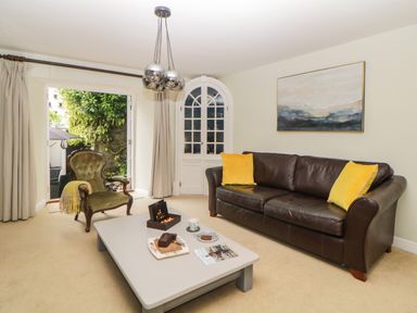 A living room with a leather sofa with yellow cushions an armchair a coffee table and large windows at Lower Culvermead in Chaddlehanger near Tavistock