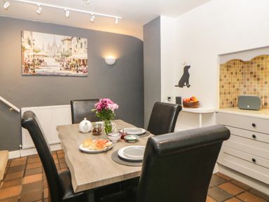 A dining area with a wooden table set for breakfast with black chairs and a kitchen countertop with tiled backsplash at Lower Culvermead in Chaddlehanger near Tavistock
