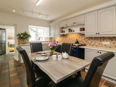 A kitchen with a wooden dining table set for two with plates cups a teapot and flowers in a vase and white cabinets with a tiled backsplash at Lower Culvermead in Chaddlehanger near Tavistock