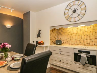 A kitchen with a dining table with plates and flowers and a wall clock above a tiled backsplash at Lower Culvermead in Chaddlehanger near Tavistock