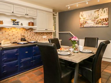 A kitchen with a blue stove brown tiled floor and a dining table set for four with flowers at Lower Culvermead Chaddlehanger near Tavistock