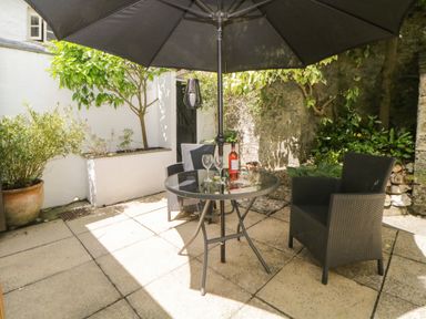 An outdoor patio with a round glass table under a black umbrella two black woven chairs plants and trees around Lower Culvermead Chaddlehanger near Tavistock